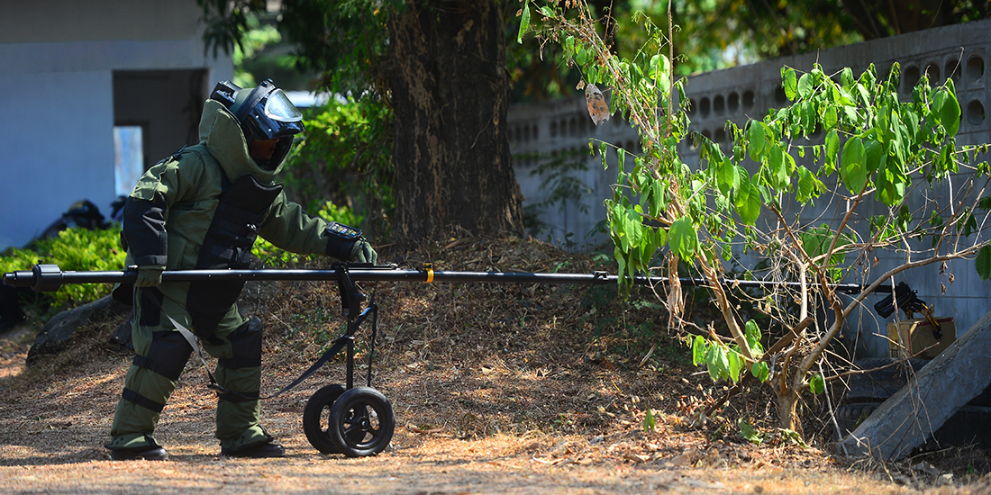 EOD officer in the explosive ordnance disposal suit using remote robot hand to check the unclear box beside the wall